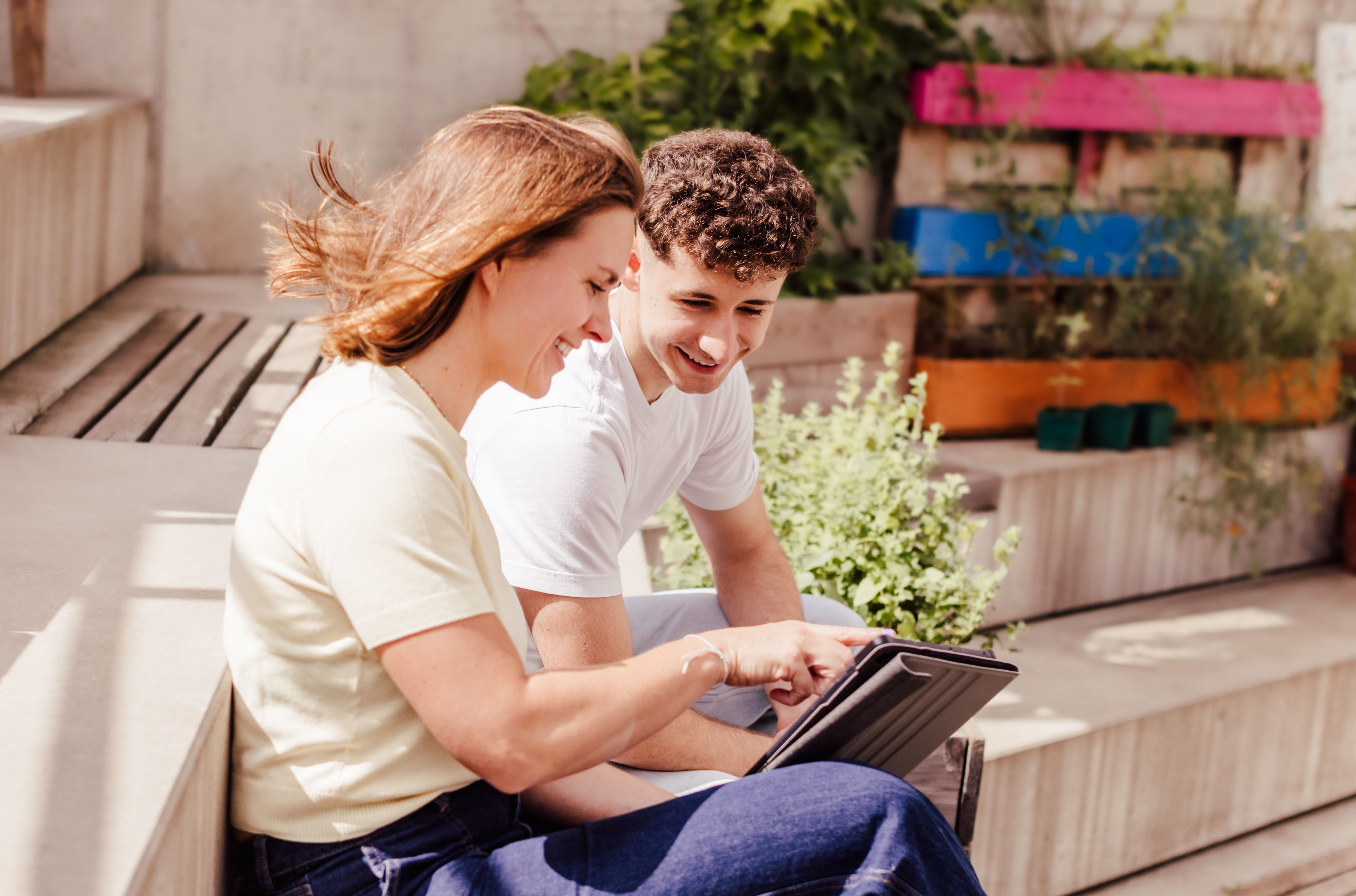 Beratungssituation draußen in einem Innenhof: eine Beraterin zeigt einem Jugendlichen etwas auf einem Tablet;