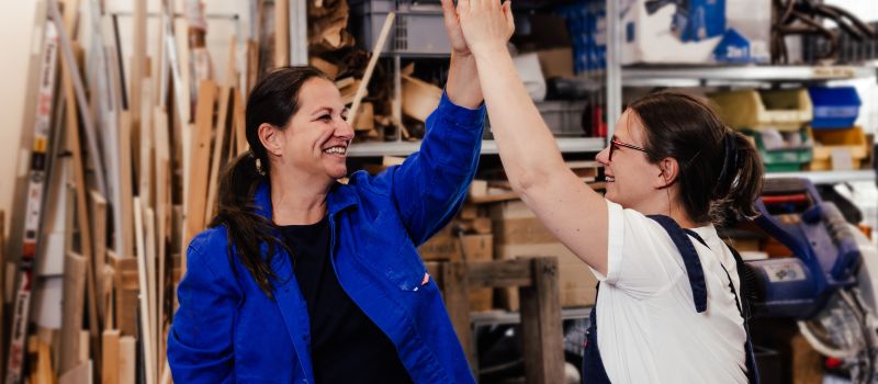 Tischlerin mit weiblichem Coach, die zwei Frauen schlagen ein und lachen.