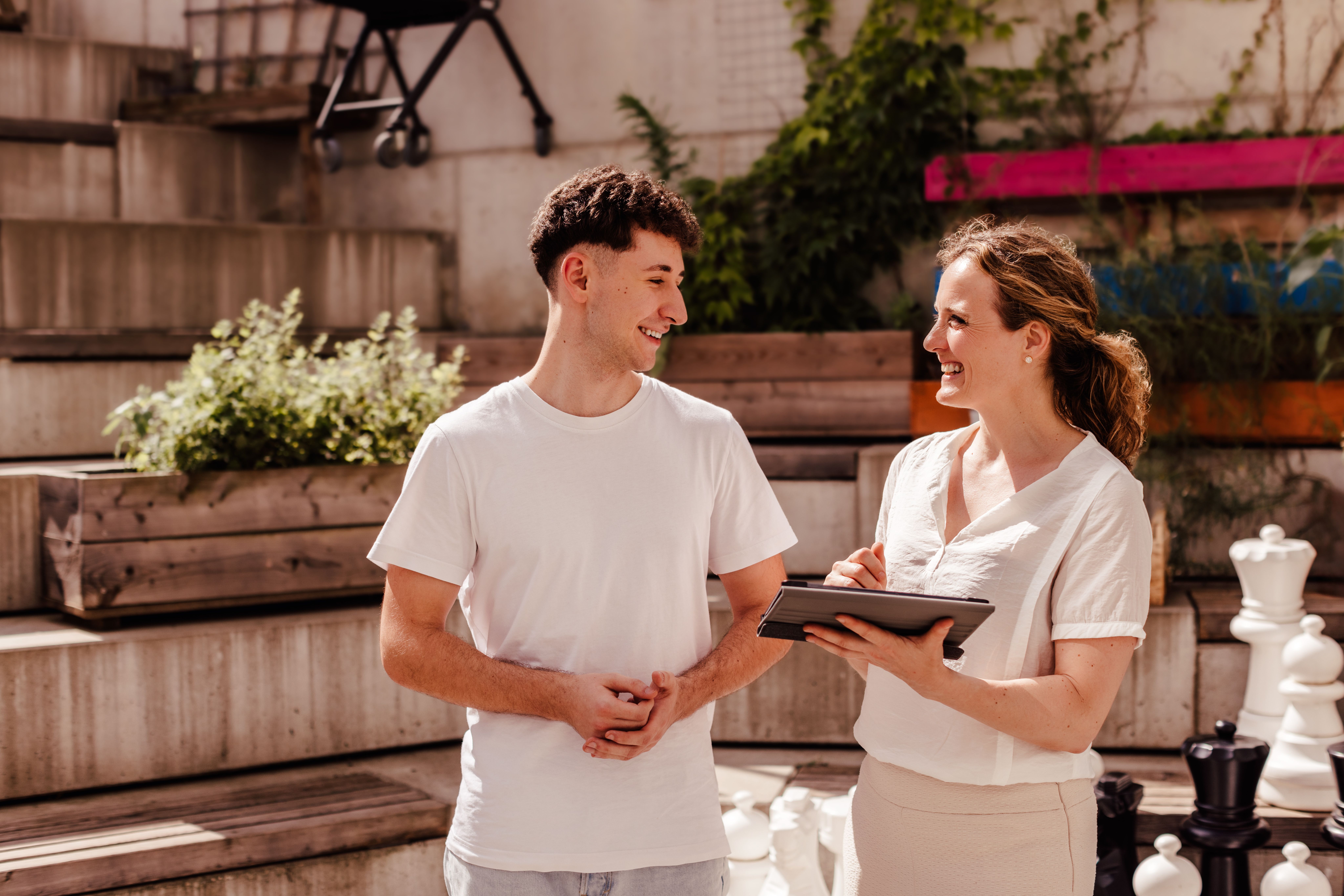 Beratungssituation: eine junge Frau sitzt lächelnd gegenüber einem Betreuer in einem Büro. Auf dem Schreibtisch liegen Unterlagen und im Hintergrund ist ein Bild mit Sonnenblumen zu sehen.